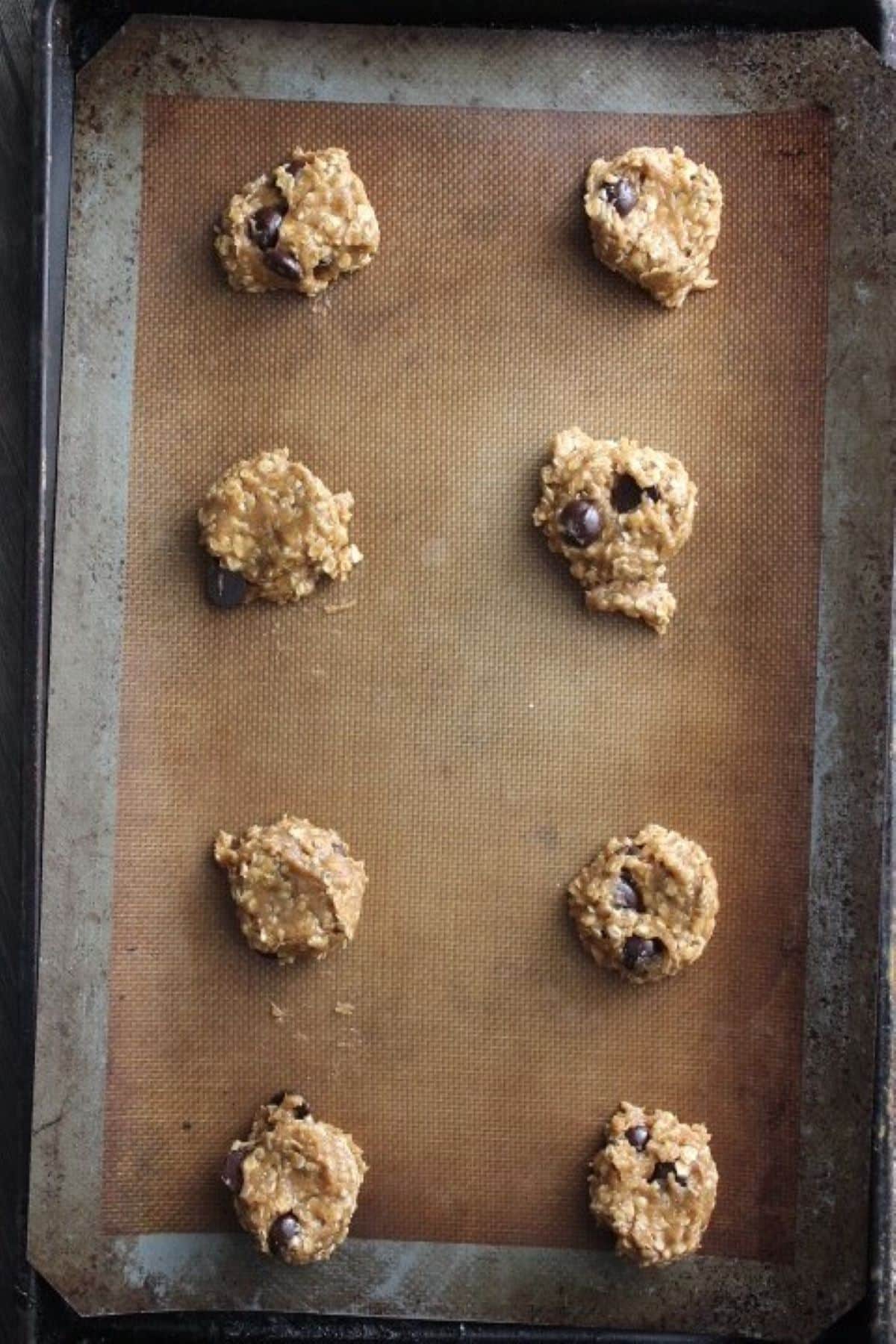 Image of raw pumpkin oatmeal chocolate chip cookie dough portioned into table spoon-sized balls onto baking sheet.